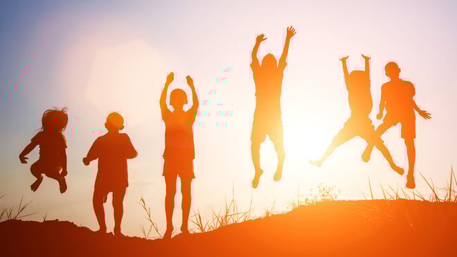 Silhouet af børn der hopper i solnedgangen. Sommerferie for trængte familier.