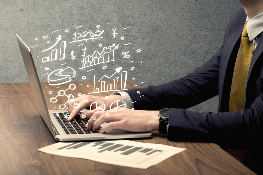 Sales person in suit using a laptop to calculate pie chart and exponential growth statistics on office desk concept